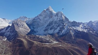 Nangkarshang Tepesi 'nde zaferle ayakta duran dağcı, Ama Dablam dağının arkasında yükseliyor, tırmanma başarısını ve dağlık yaban hayatını ifade ediyor..