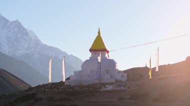 Güneş ışığını yansıtan altın tepecik, dans eden bayraklar, kutsal anıtın arkasında yükselen kar örtülü Everest Dağı..