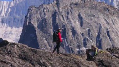 Nangkarshang Tepesi 'nde dik kayalıklardan geçen dağcı, parlak alp ışığı altında uzak buzul arazisiyle çelişen kırmızı ceket..