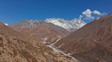 Himalaya 'nın engebeli arazisinin üzerinde yükselen devasa Everest Dağı, karla kaplı zirve delen gökyüzü, el değmemiş Nepal çöllerindeki dramatik vadiyi gözler önüne seriyor..