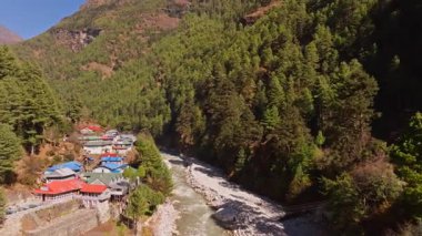 Ürdün yakınlarındaki yemyeşil vadide kıvrılan çalkantılı dağ nehrinin hava manzarası, Himalaya 'nın yemyeşil orman manzarasının ortasında yuva yapmış..