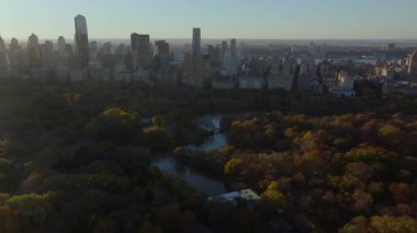 Sıcak sabah ışığı Central Park 'ı ve Manhattan şehir merkezini sarar, binalardan ve sonbahar ağaçlarından gölgeler bırakır, New York' un sakin şehir atmosferini.