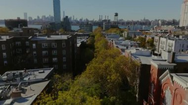 Williamsburg, Brooklyn 'de tuğla binaların yer aldığı ağaçların üzerinde süzülen hava manzaralı arka planda East River ve Manhattan silueti görünür..