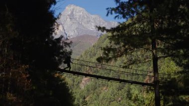 Nepal 'deki dağ yürüyüşü sırasında Jorsalle' deki Himalaya vadisinde ahşap asma köprüyü geçen yalnız bir yürüyüşçü..