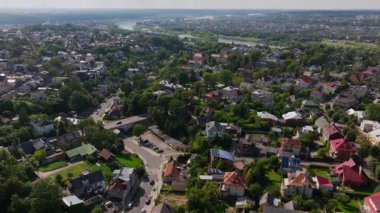 Kaunas, Litvanya üzerinde gezinirken, evlerle dolu büyüleyici bir mahalle, nehir boyunca uzanan bir köprü ve güneşli bir gökyüzü altında yemyeşil bir yer sergiliyor..