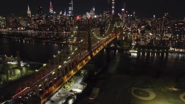 Manhattan ve Queens 'i Doğu Nehri' ne bağlayan aydınlanmış Queensboro Köprüsü 'nün gece hava görüntüsü. Arabalar köprüden geçer ve arka planda Manhattan ışıkları parlar..