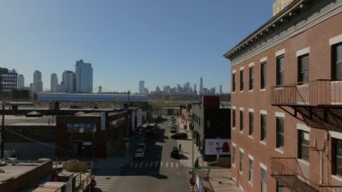 Brooklyn 'de tipik bir Williamsburg caddesinde havada süzülen hava manzarası. Her iki tarafta kırmızı tuğlalı binalar var. Park halindeki arabalar ve arka planda yükselen Manhattan silueti..