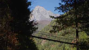 Jorsalle 'deki engebeli dağ vadisine uzanan dar asma köprüden geçen maceraperest bir gezgin, Nepal Himalaya yürüyüşünün özünü yakalıyor..