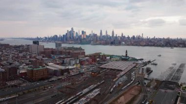 Hoboken Terminali, Manhattan silueti bulutlu gökyüzünün altında Hudson Nehri 'nden yükseliyor, New Jersey ulaşım ağını aydınlatıyor..