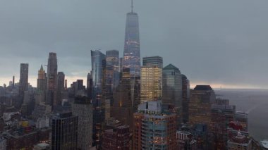 Aşağı Manhattan silueti alacakaranlıkta ortaya çıkıyor. Bir Dünya Ticaret Merkezi, aydınlık şehir ışıklarıyla karanlık şehir manzarasına karşı belirgin bir şekilde duruyor..
