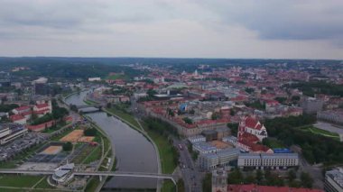 Bulutlu bir günde Vilnius 'tan akan Neris Nehri şehirlerin kırmızı çatılarını ve kiliselerini vurgular ve kentsel bir ortamda tarihi ve kültürün büyüleyici bir karışımını yaratır..