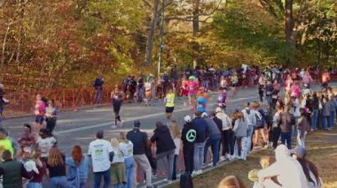 Maraton koşucuları, canlı bir sonbahar sabahı renkli Central Park caddesi boyunca tezahürat yapan seyircilerin yanından geçiyor. NYC, ABD, 11.5.2024.