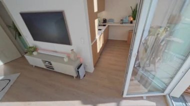 Uzaktan kumandayı bitiren adam, güncel apartman mutfağında günışığı penceresinin yanında kahve demleyen, dizüstü bilgisayar kapayan, Berlin, 5.8.2025.