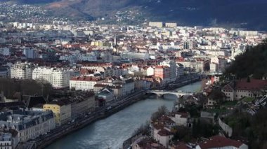 Grenoble şehir manzarasının hava manzarası, Isere Nehri 'nin şehir arazisini iplikçiklediğini, dağlık alanlar arasındaki mimari alanları birbirine bağladığını gösteriyor..