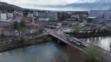 Grenoble şehri, arka planda tramvaylar, araba trafiği, binalar ve dağlarla dolu bir köprü olan Isere nehrinin manzarası..