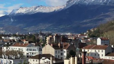 Panoramik şehir manzarası Grenobles 'ın çatılarını yakalıyor. Parlak, bulutsuz gökyüzü altındaki yüksek Fransız Alpleri tarafından çerçevelenmiş konutlar..