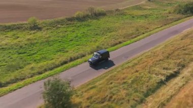 Siyah SUV, yemyeşil çayırlarla çevrili asfalt bir yol boyunca gidiyor. Sahne, doğa ve sükunetin güzelliğini gösteren kırsal manzaraların özünü yakalıyor. Berlin, Almanya 5 Temmuz