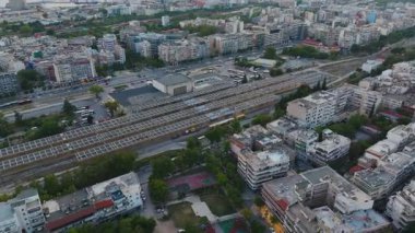 Hava görüntülerinde Selanik 'in canlı şehir merkezi, bir tren istasyonu, hareketli yollar ve güneşli bir yaz gökyüzü altında modern ve tarihi binaların karışımı yer alıyor..