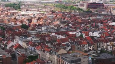 Kentsel manzara, ikonik kırmızı çatılarıyla Brüksel 'i vurguluyor. Güneşli bir yaz gününde, bir tren uzak raylar boyunca süzülür, canlı atmosferi güçlendirir..