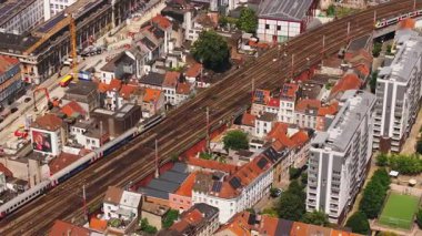 Tren Brüksel 'deki bir istasyona yaklaşıyor. Binaları, tren rayları ve devam eden kentsel gelişimi ile şehir manzarası sunuyor..