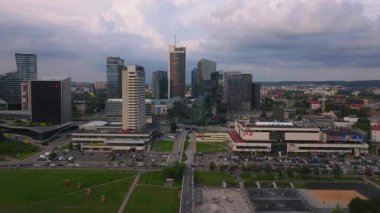 Kamera Vilnius, Litvanya 'daki modern ticaret bölgesini gösteriyor. Şehir manzarasında gökdelenler, ofis binaları ve yeşil alanlar yer alıyor..