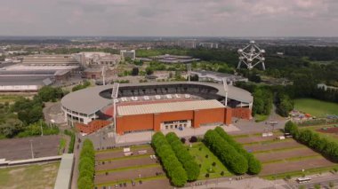Brüksel 'in Heysel ilçesindeki King Baudouin Stadyumu hava gösteriminde, Belçika milli futbol takımının evi, yemyeşil ağaçlar ve bulutlu gökyüzü altındaki kentsel binalarla çevrili..