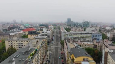 Arabalar Brno 'da çağdaş binalarla dolu geniş bir caddede yol alıyorlar. Şehir manzarası hareketli şehir dinamiklerini yakalıyor, trafik bulutlu bir gökyüzünün altında durmadan hareket ediyor..