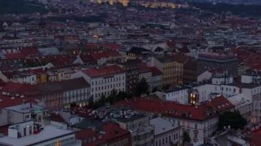 Prag çatıları mavi saat boyunca ışıldıyor, zarif mimari ve canlı şehir ışıklarını vurguluyor, muhteşem Prag Kalesi arka planda belirgin bir şekilde yükseliyor..