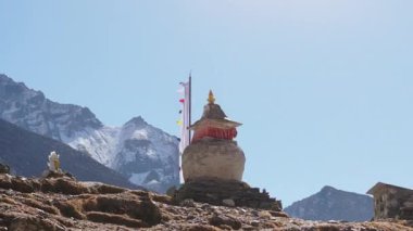 Huzurlu bir Nepal manzarası, heybetli kar örtülü dağların zemininde dua bayraklarıyla süslenmiş, sersemletici bir yapı..
