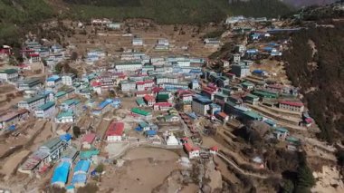 Nepal dağlarında yuva yapmış uzak bir köyün havadan görünüşü, ağaçlar sergileniyor ve arka planda görkemli bir kar tepesi var..