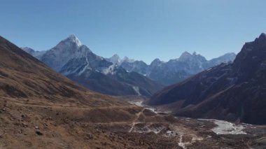 Himalayalar 'ın Nepal' deki nefes kesici manzarası, kayalık bir patikada, karlı tepeler ve dingin bir buzul vadisi arasında bir yürüyüşçüyü gösteriyor..