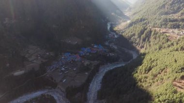 Nepal dağlarına kurulmuş sakin bir köyün havadan görünüşü geleneksel mimariyi ve kıvrımlı bir nehri gösteriyor..