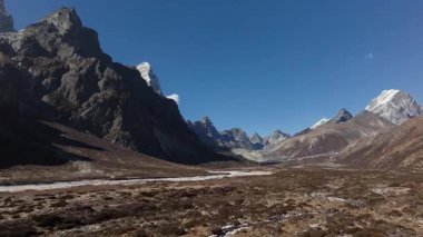 Nepal 'deki uzak bir dağ vadisinin havadan görünüşü, açık mavi gökyüzünün altında karla kaplı tepeler ve dolambaçlı bir nehir..
