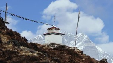 Renkli dua bayraklarıyla süslenmiş, Nepal 'deki görkemli karlı dağların zeminine kurulmuş beyaz bir stupa manzarası..