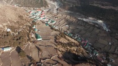 Gözlerden uzak bir Nepal köyünün yukarıdan çekimleri, kırsal binalar ve büyük bir karlı zirve.