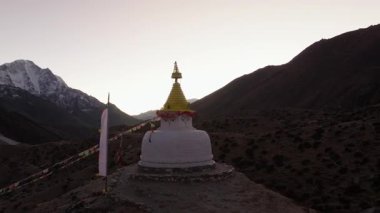 Himalayalar 'da yuva yapmış sakin bir Nepalli köyünün hava manzarasında, gün batımında görkemli bir stupa ve karla kaplı dağlar yer alıyor..