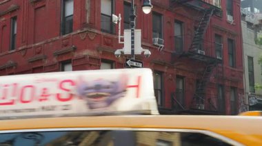 Hareketli bir New York kavşağının statik görüntüsü, ikonik kırmızı tuğla binalar ve sarı bir taksi..
