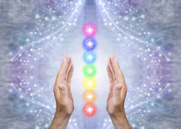 Sensing Seven Chakras and Sending Healing - Male parallel hands with 7 rainbow coloured energy centres between against a blue flowing sparkling background and copy space 