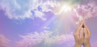 Praying to Divine Intelligence up there in the heavens above - male hands in prayer position against a beautiful pink blue sky with fluffy clouds and the sun behind sending rays of light down with copy space