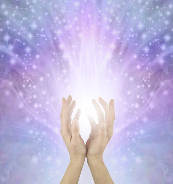 There is enough healing energy for everyone - Female Reiki Master Healer with cupped hands sending out vast amounts of white starlight against beautiful pink blue energy field background and copy space