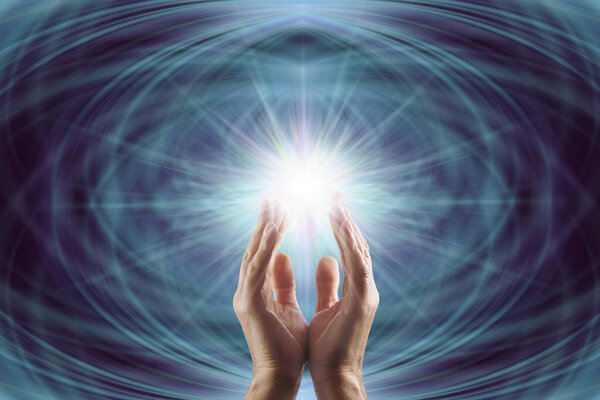 Reiki master working with Starlight Healing Energy - male cupped hands reaching up into bright white light starburst  against a dark blue symmetrical ethereal background and copy space