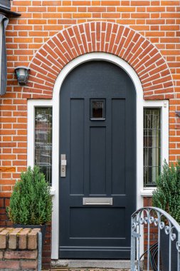 Bir evin ahşap ön kapısı. Pencereli tuğladan bir evin ahşap bir ön kapısının önünde. Bitkiler ve geniş bir veranda ve ön geçit manzarası. Yatay çekim.