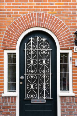 Bir evin ahşap ön kapısı. Pencereli tuğladan bir evin ahşap bir ön kapısının önünde. Bitkiler ve geniş bir veranda ve ön geçit manzarası. Yatay çekim.