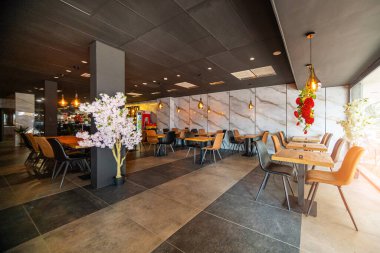 Modern ve zarif bir yemek alanı sunan güzel tasarlanmış bir restoran iç mekanı. Uzay, ahşap sandalyeler ve cam kaplamalı masalar da dahil olmak üzere çağdaş mobilyalara sahip..