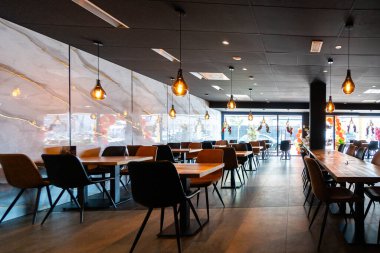 Konforlu ve modern kafe içi ahşap mobilyalar, sıcak ışıklandırma ve sokağa bakan büyük pencerelerle, davetkar bir atmosfer yaratıyor.