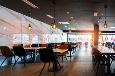 Konforlu ve modern kafe içi ahşap mobilyalar, sıcak ışıklandırma ve sokağa bakan büyük pencerelerle, davetkar bir atmosfer yaratıyor.