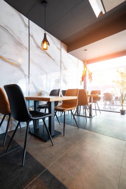 Konforlu ve modern kafe içi ahşap mobilyalar, sıcak ışıklandırma ve sokağa bakan büyük pencerelerle, davetkar bir atmosfer yaratıyor.