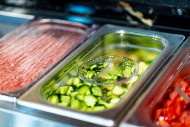 Profesyonel mutfak ortamında çeşitli sebze ve malzemelerle dolu metal kaplar, dikey görüntü.