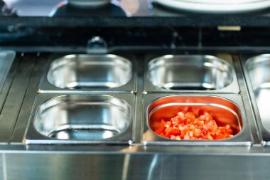 Profesyonel mutfak ortamında çeşitli sebze ve malzemelerle dolu metal kaplar, dikey görüntü.