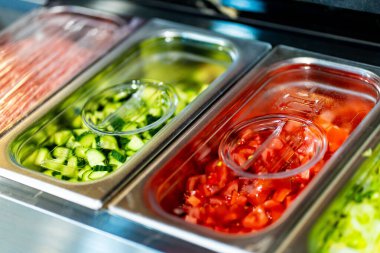 Profesyonel mutfak ortamında çeşitli sebze ve malzemelerle dolu metal kaplar, dikey görüntü.